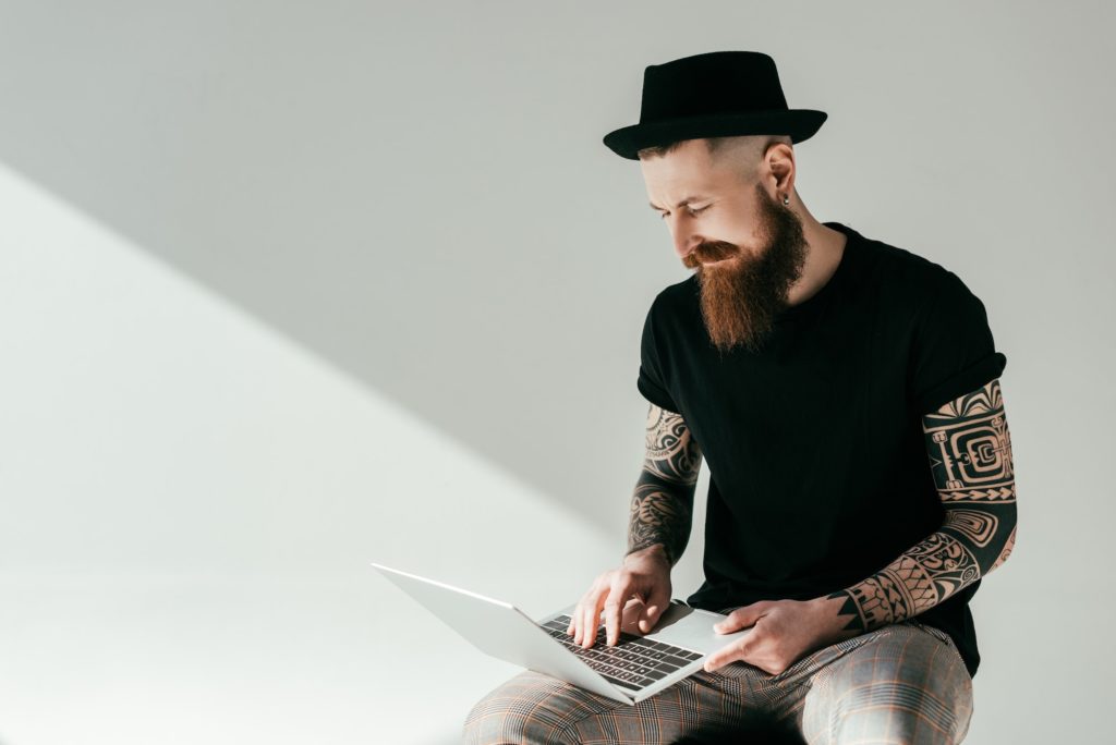 handsome bearded tattooed man looking at laptop on white